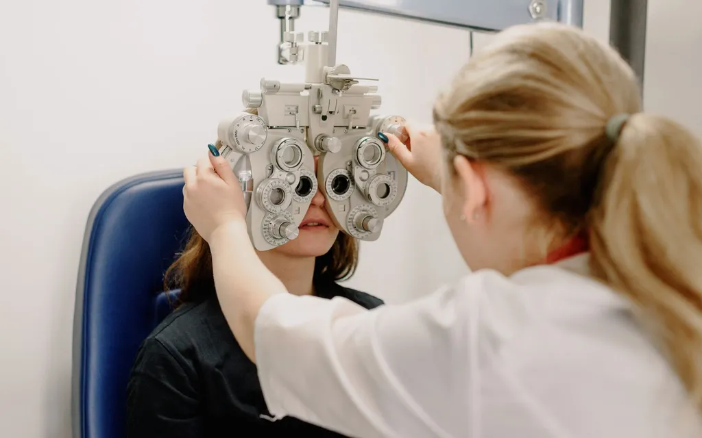 Optometrist adjusting a phoropter while testing a patient's vision during an eye examination