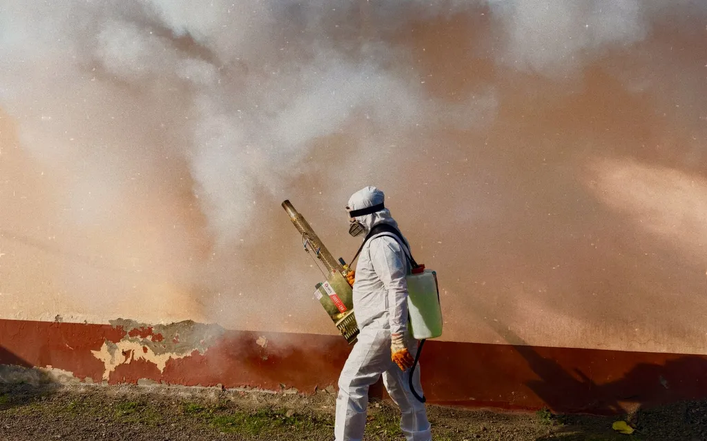 Pest control technician in a white protective suit and respirator fogging the exterior of a property