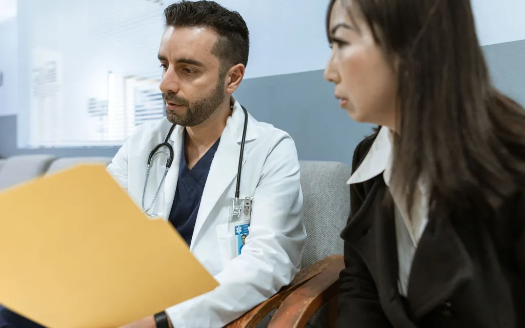 A private GP with a stethoscope reviewing notes with a patient in a clinic consultation