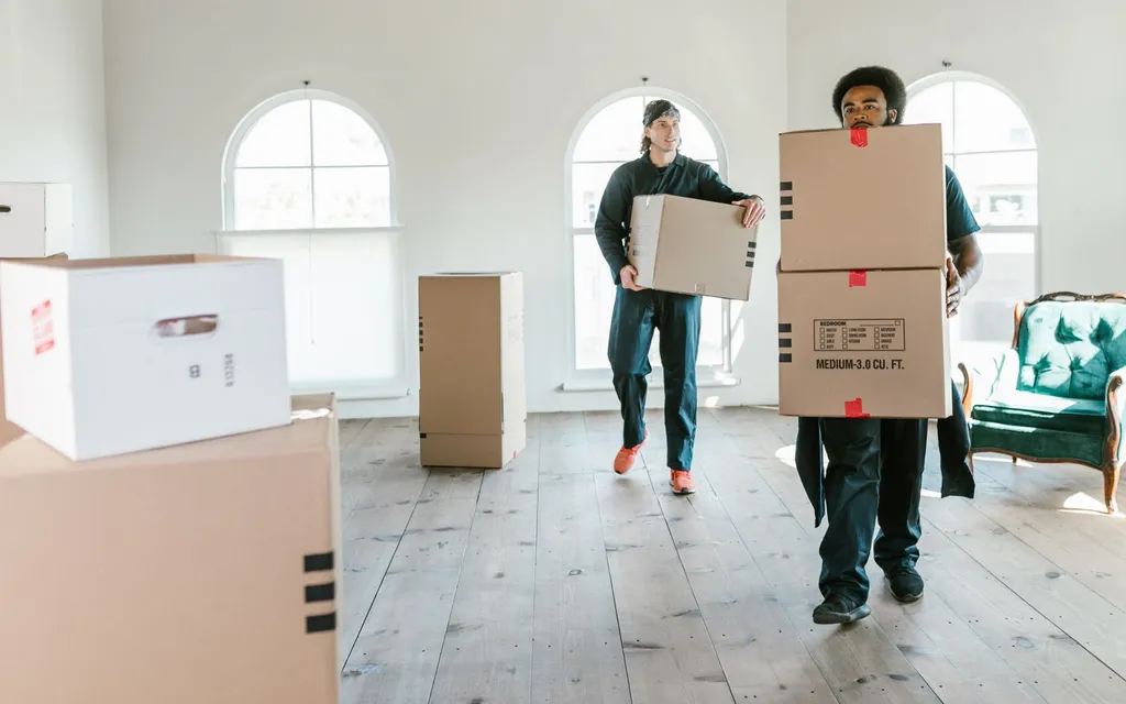 Removals crew carrying cardboard boxes through a bright empty room
